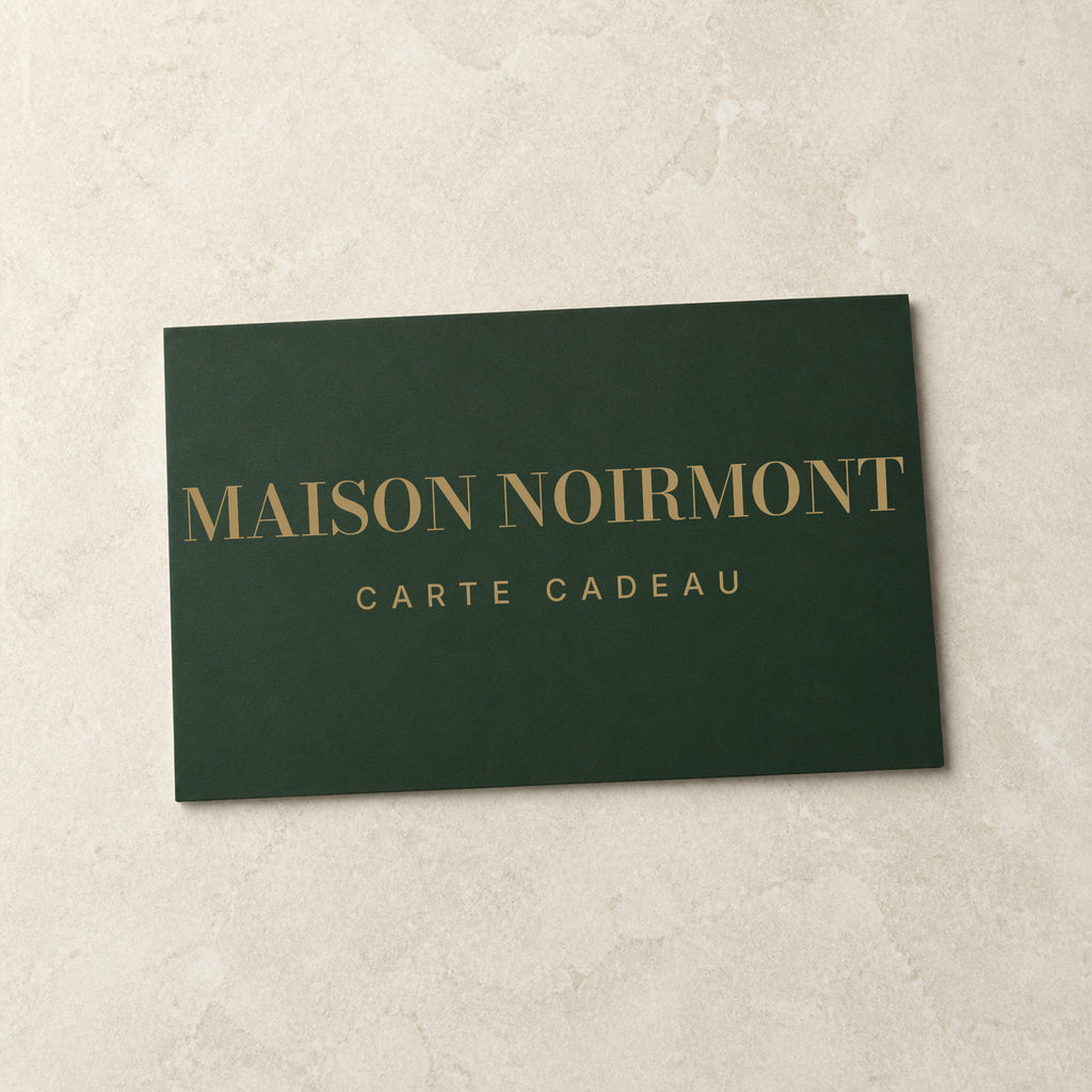 Carte cadeau Maison Noirmont — carte vert jura marquée laiton, posée sur pierre claire