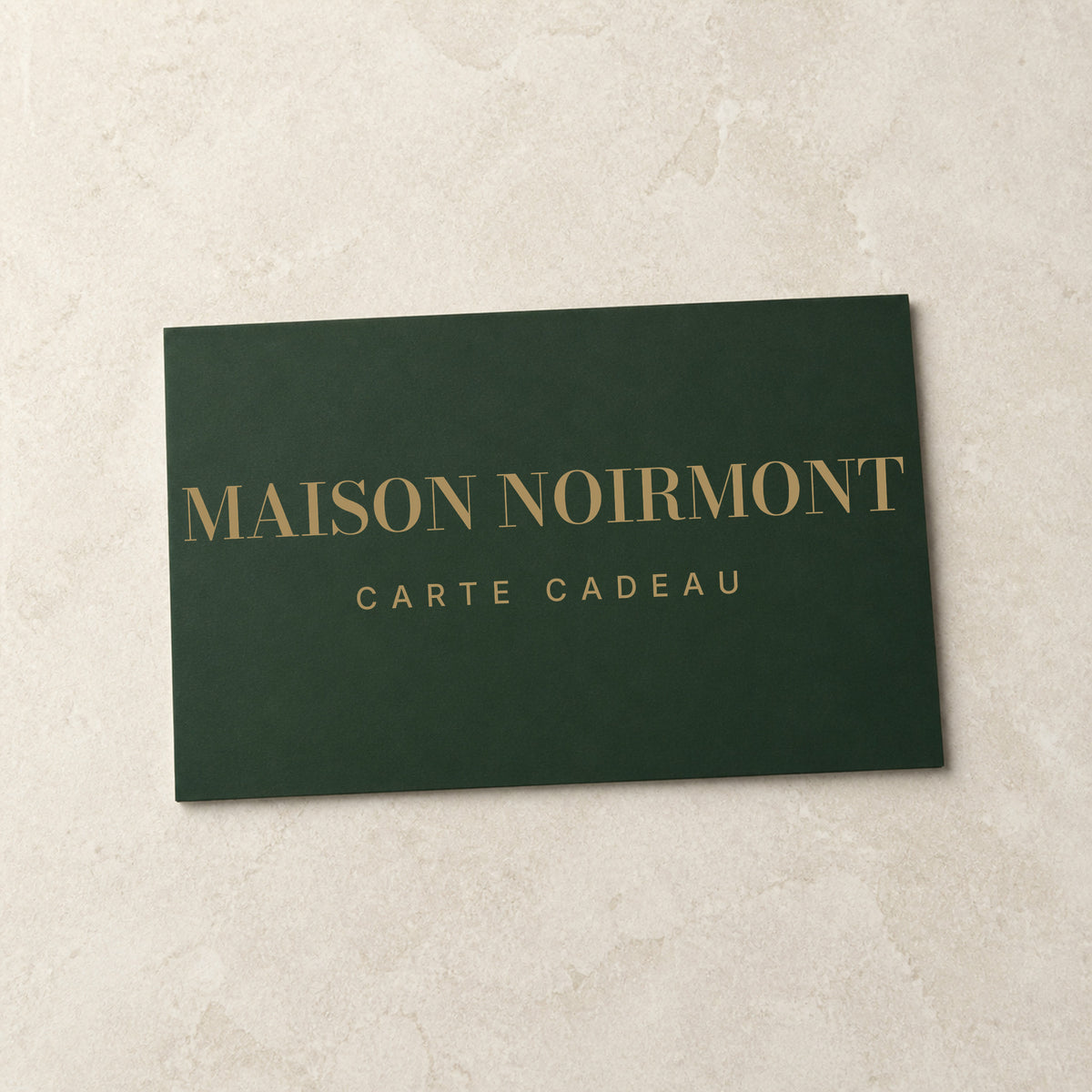 Carte cadeau Maison Noirmont — carte vert jura marquée laiton, posée sur pierre claire