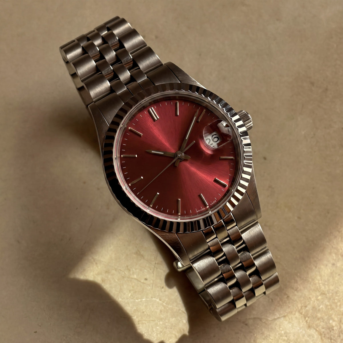 Trente-Neuf — cadran rouge soleillé, index bâtons appliqués, lunette cannelée acier et bracelet cinq rangs — Maison Noirmont