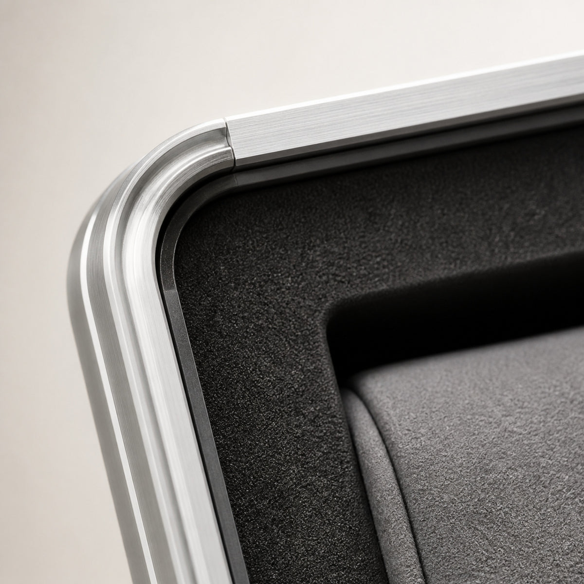 Coffret Douze — macro de l'angle : profil en aluminium brossé à arrête arrondie, insert intérieur noir texturé et bord d'un coussin gris — Maison Noirmont