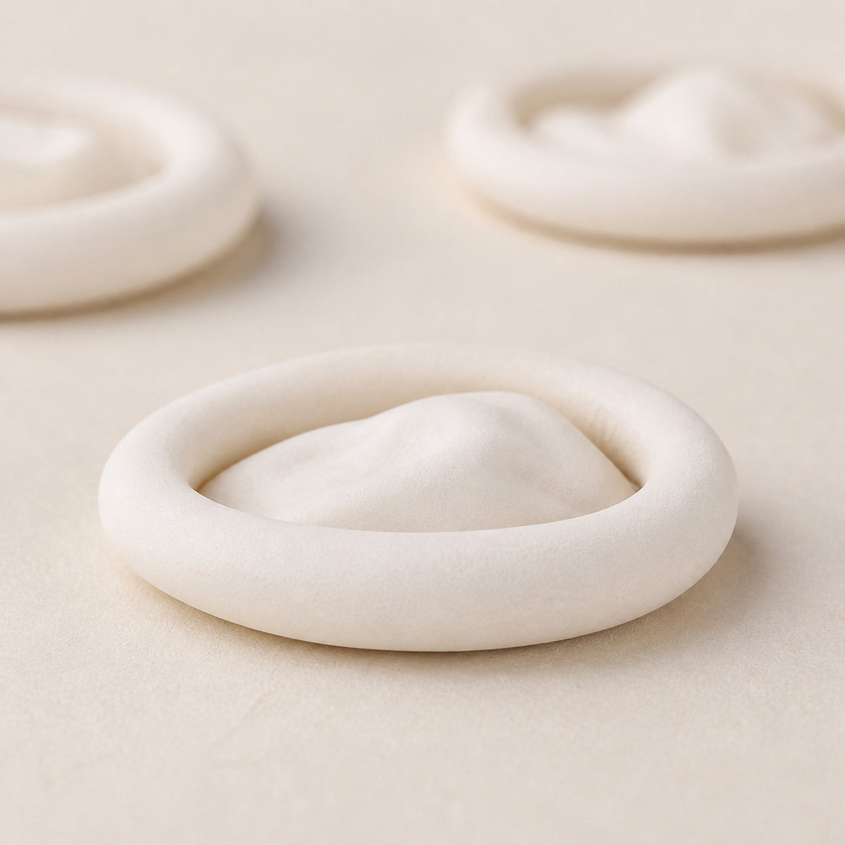 Doigtiers d'horloger — macro d'un doigtier en latex blanc cassé mat, conservé roulé sur son bourrelet, deux autres en arrière-plan — Maison Noirmont