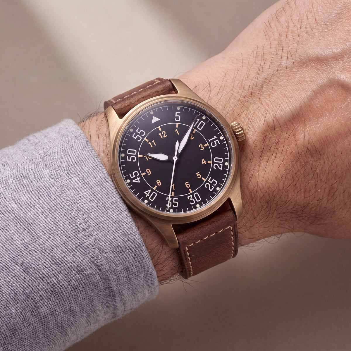 Noirmont Un Bronze — Aviateur bronze porté au poignet sur bracelet cuir brun surpiqû écru — Maison Noirmont