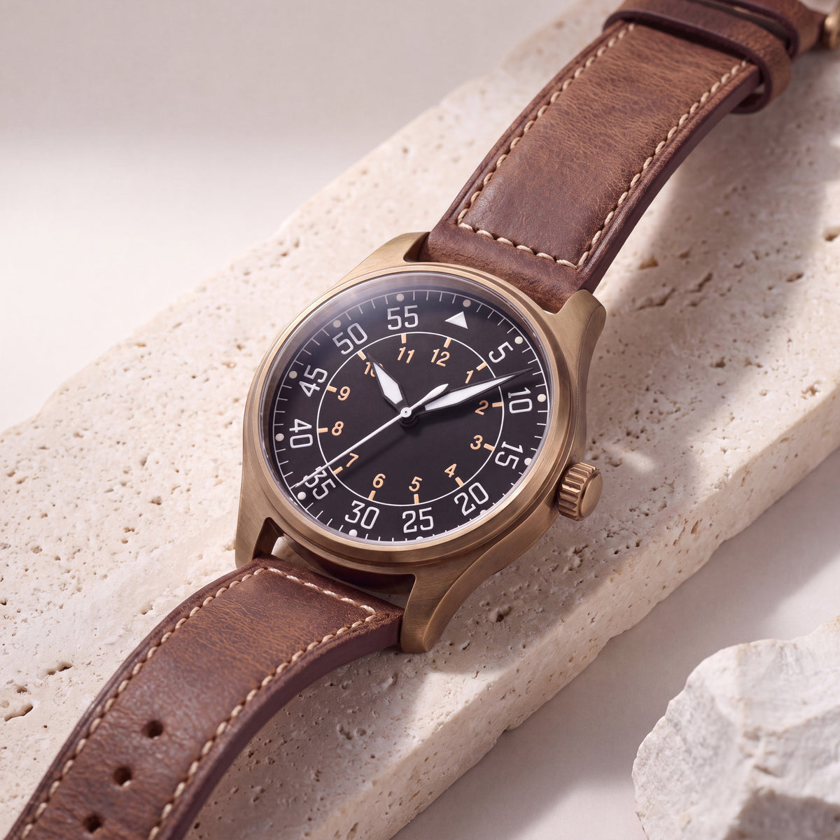 Noirmont Un Bronze — Aviateur bronze à chiffres 1-12, posé de trois quarts sur pierre claire, bracelet cuir brun — Maison Noirmont