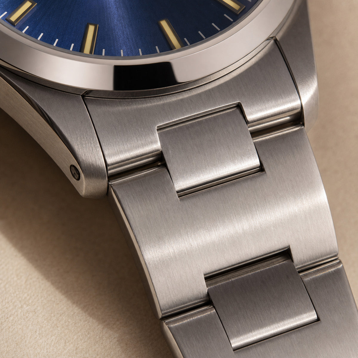 Quarante-et-Un Bleu Acier — macro de la jonction boîtier-bracelet : premiers maillons acier étagés brossés et polis, cadran bleu roi soleillé à index dorés en haut de cadre — Maison Noirmont