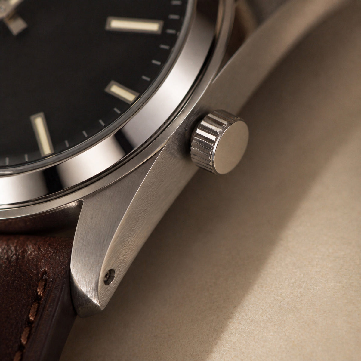 Quarante-et-Un Noir — macro du profil droit : couronne cannelée non protégée, corne acier brossée à vis, cadran noir et amorce du bracelet cuir brun foncé — Maison Noirmont