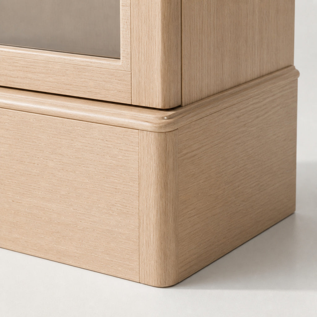 Remontoir Collection Bois beige — macro du socle : bois blond à grain droit, ressaut de plinthe arrondi et bas de la porte vitrée — Maison Noirmont