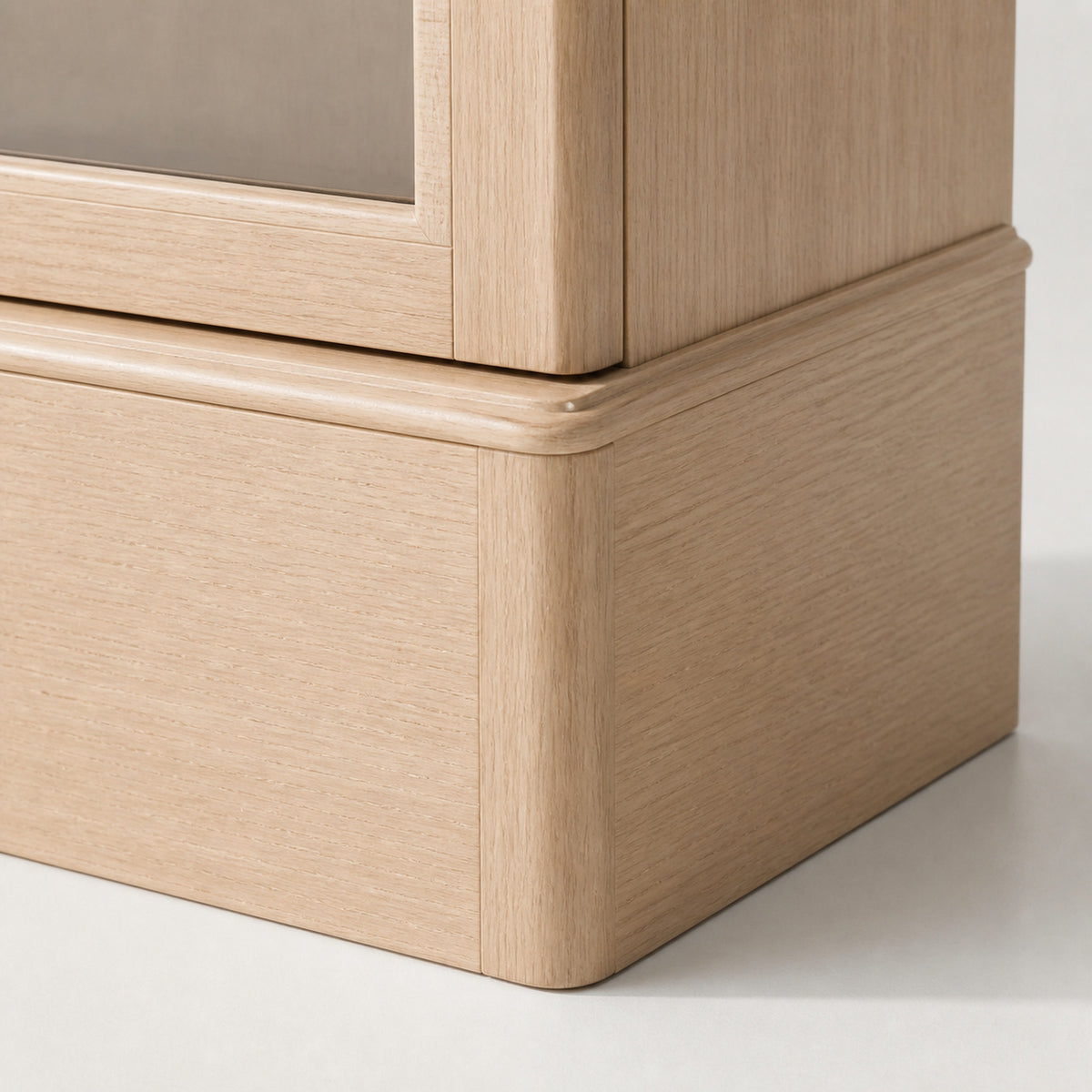 Remontoir Collection Bois beige — macro du socle : bois blond à grain droit, ressaut de plinthe arrondi et bas de la porte vitrée — Maison Noirmont