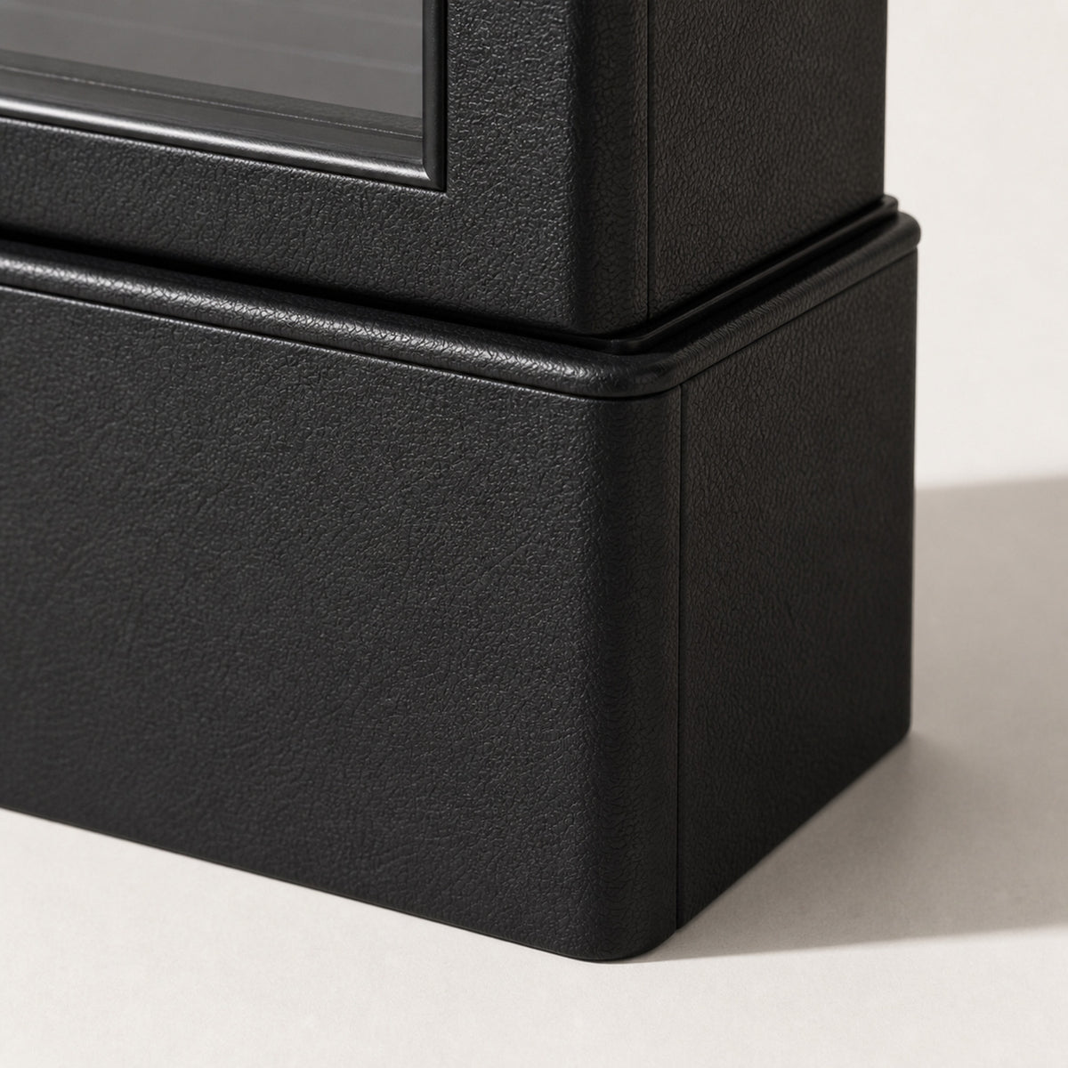 Remontoir Collection Cuir PU — macro du socle : habillage en cuir PU noir à grain fin, angle arrondi, bourrelet de transition et chant de la vitrine — Maison Noirmont
