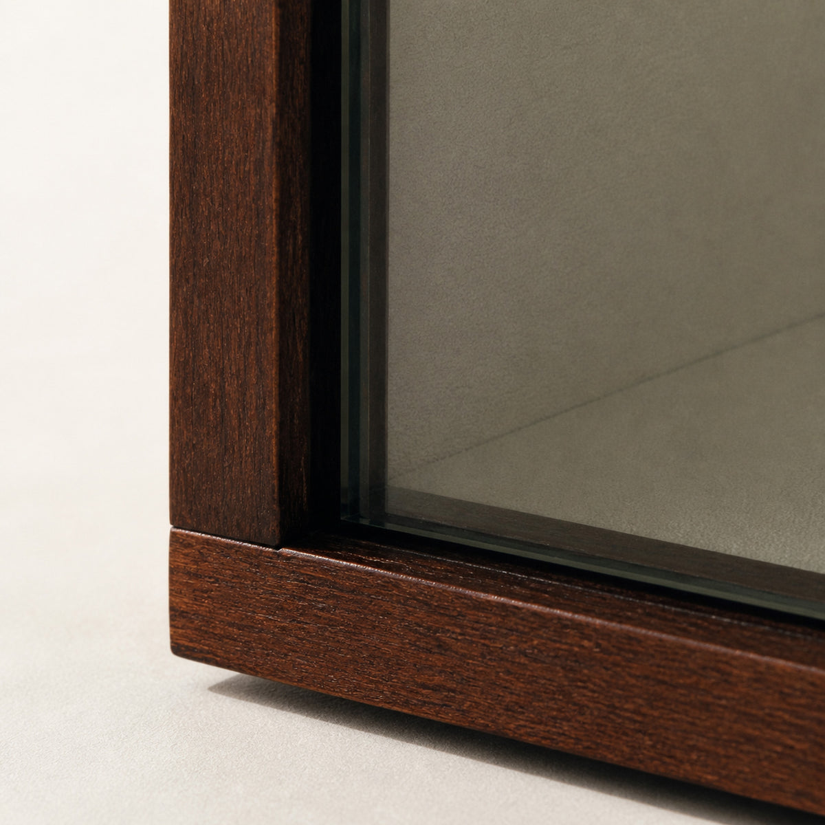 Remontoir Vitrine — macro de l'angle du cadre : montant en bois brun rouge, tranche du verre et doublure intérieure taupe — Maison Noirmont