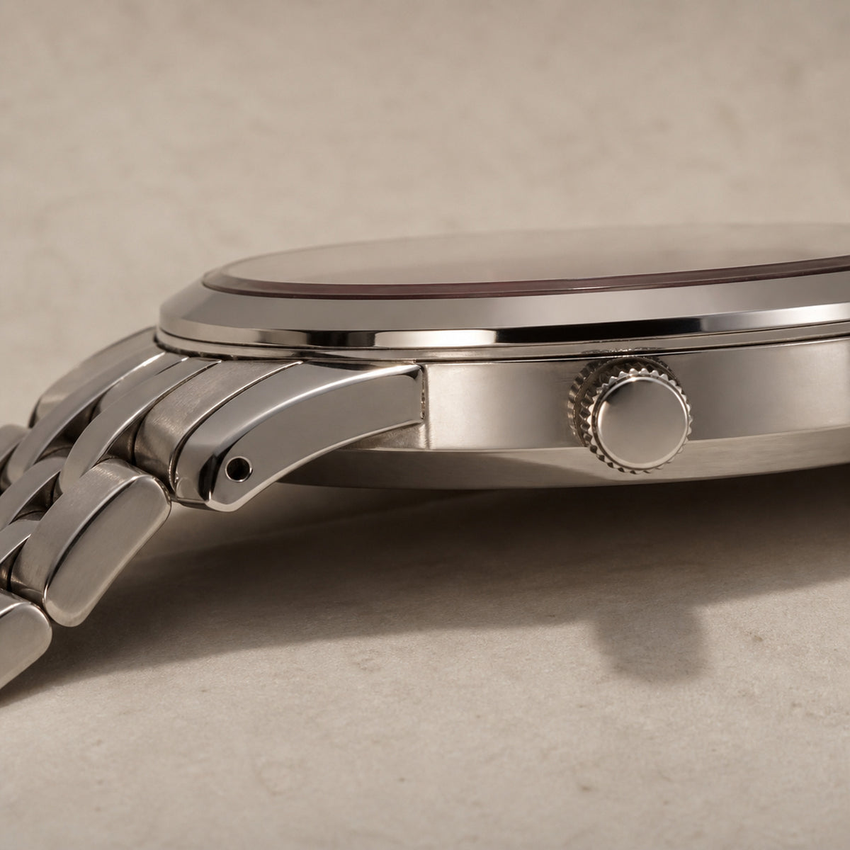 Trente-Six Rouge — profil rapproché : boîtier acier fin, couronne cannelée à sommet lisse, tranche de cadran rouge cramoisi sous le verre et première articulation du bracelet cinq rangs — Maison Noirmont